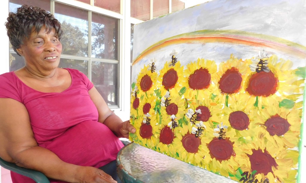 Alyne Harris displays a painting of sunflowers and bumblebees underneath a rainbow.