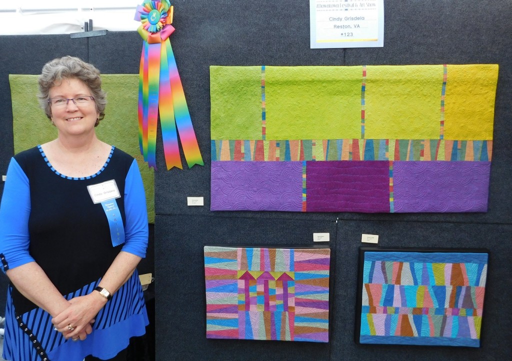 Cindy Grisdela poses with her Best In Show ribbon and her paintings titled "Promenade," top, "Skyscrapers," left, and "Waters Edge."