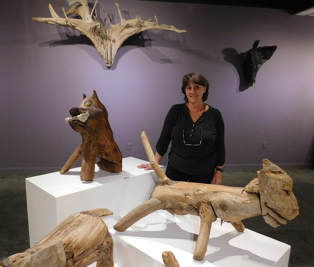 Curator Anne E. Gilroy stands among several wooden sculptures by Jesse Aaron in the Main Gallery of the Thomas Center. Photo by Gainesville Downtown)