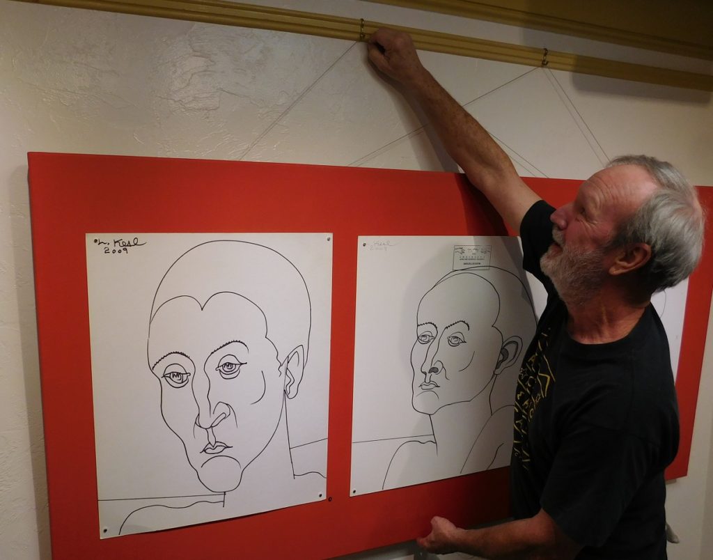 Dan Rountree adjusts a panel of Lennie Kesl line drawings on display in the "Faces of Kesl" exhibit. Photo by Gainesville Downtown)