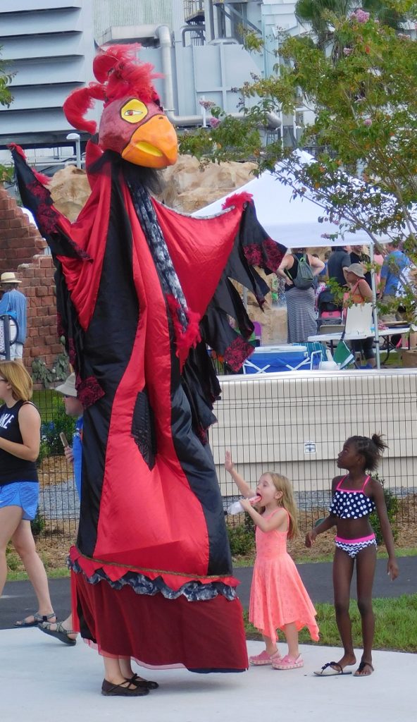 Children delight at the sight of colorful and tall bird puppet.