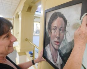 Curator Anne E. Gilroy wipes down the frame of a painting.